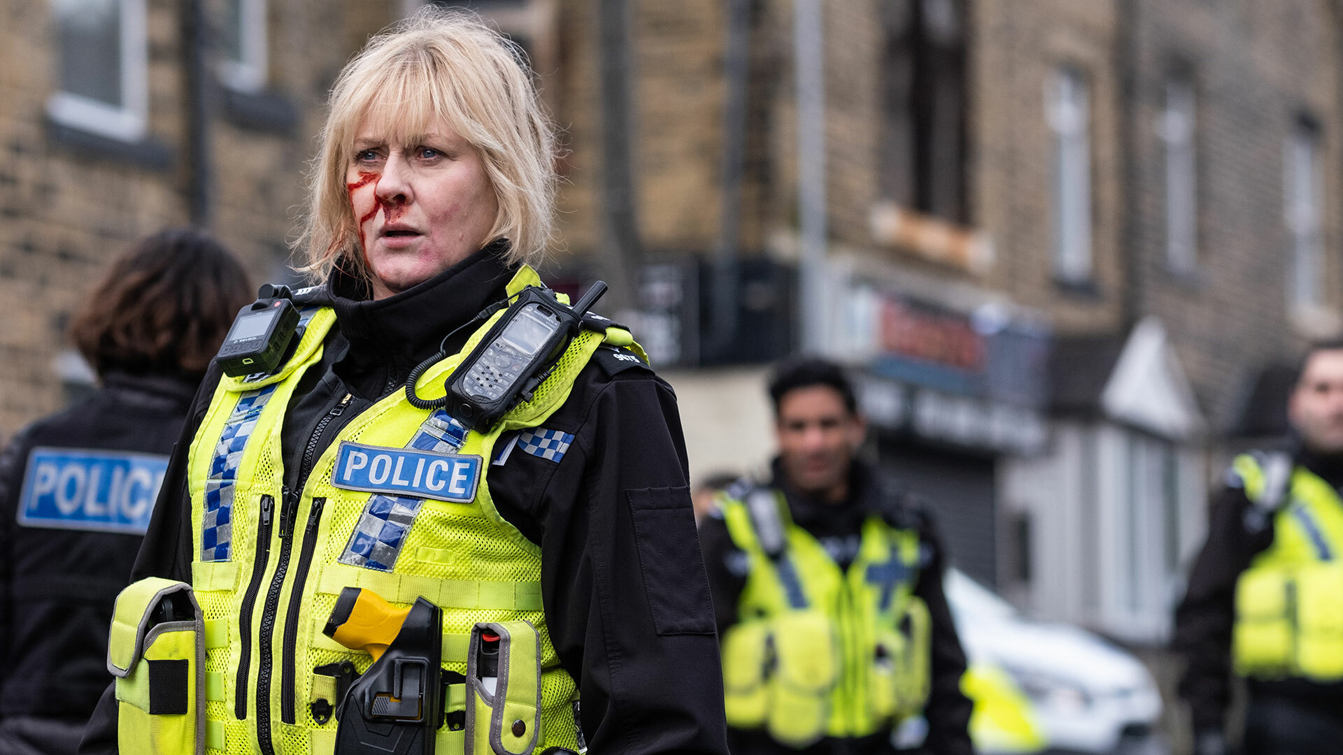 A police officer with blood on her face stands in the road with other police offers in the background.