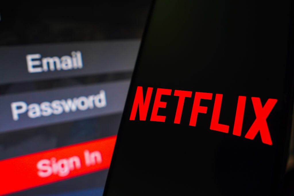 The Netflix logo is displayed on a smartphone screen, next to a login screen, with email, password, and sign in. 