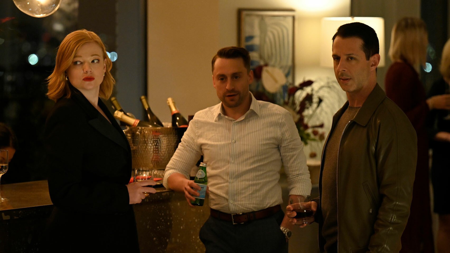 A woman and two men stand holding drinks at a party.