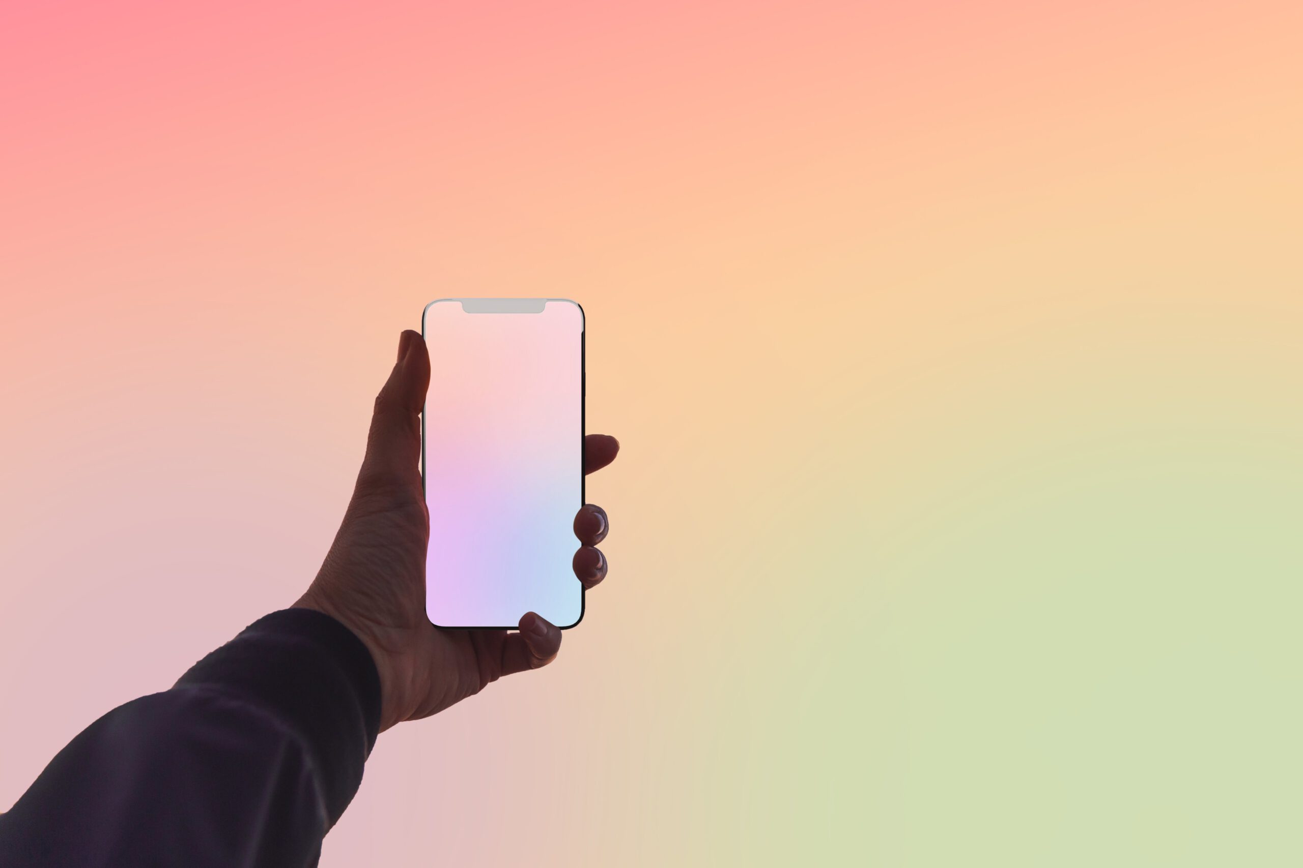 A hand holding out an iPhone in front a pink, yellow, and green gradient background.