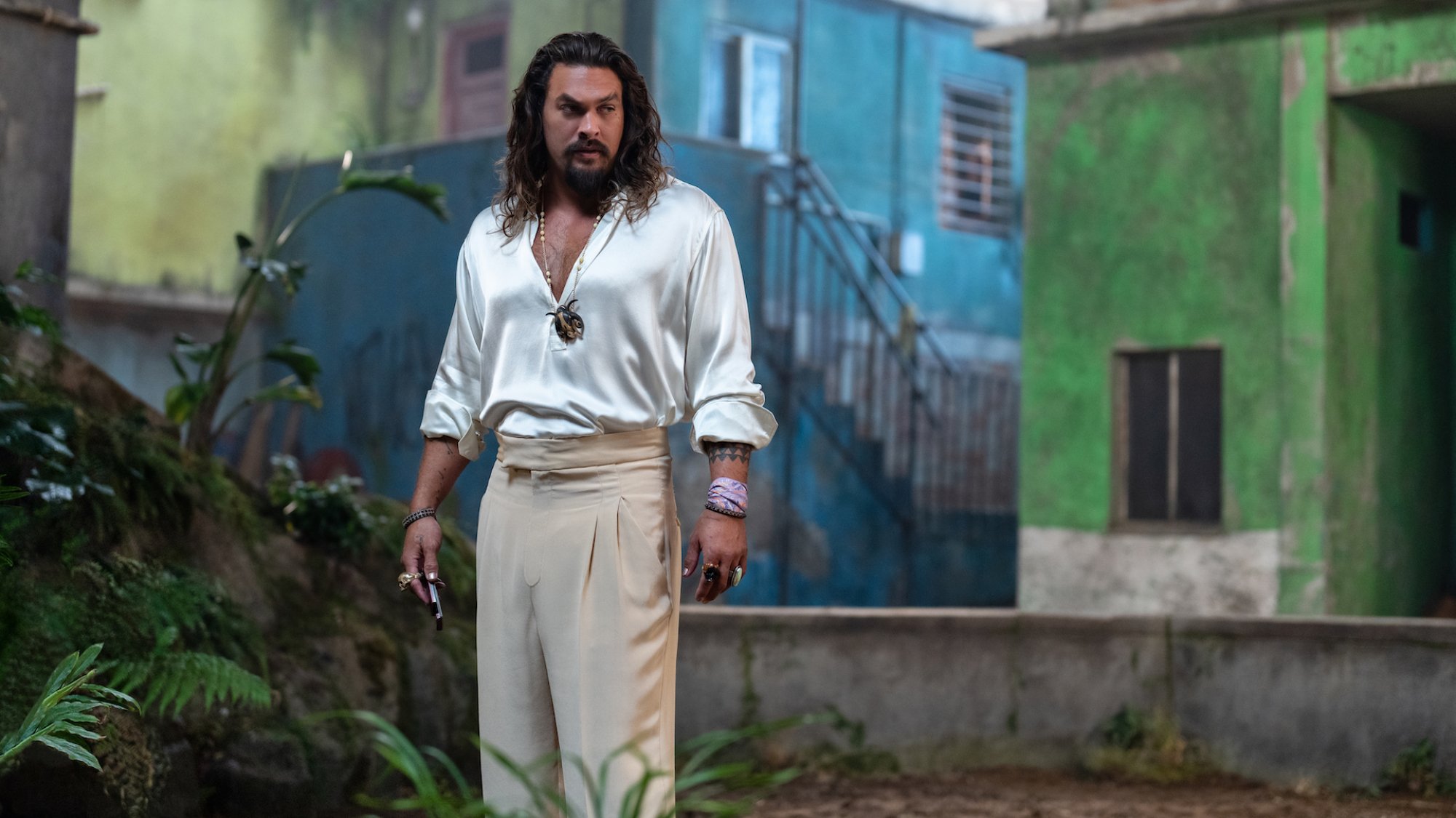 Jason Momoa stands wearing a white silk shirt and tan trousers in the film "Fast X.""