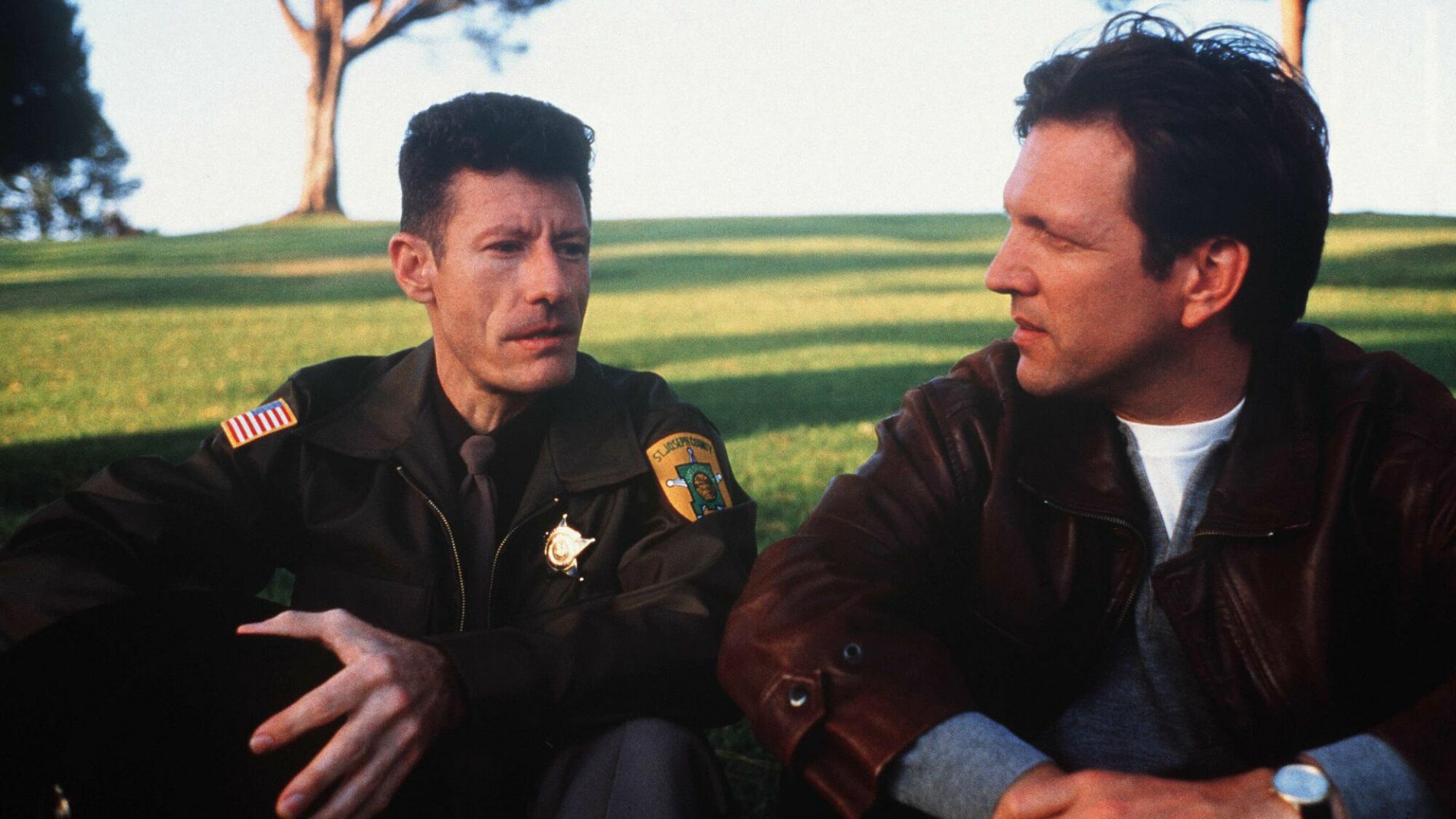 Lyle Lovett and Martin Donovan sit on a grassy knoll in "The Opposite of Sex." 