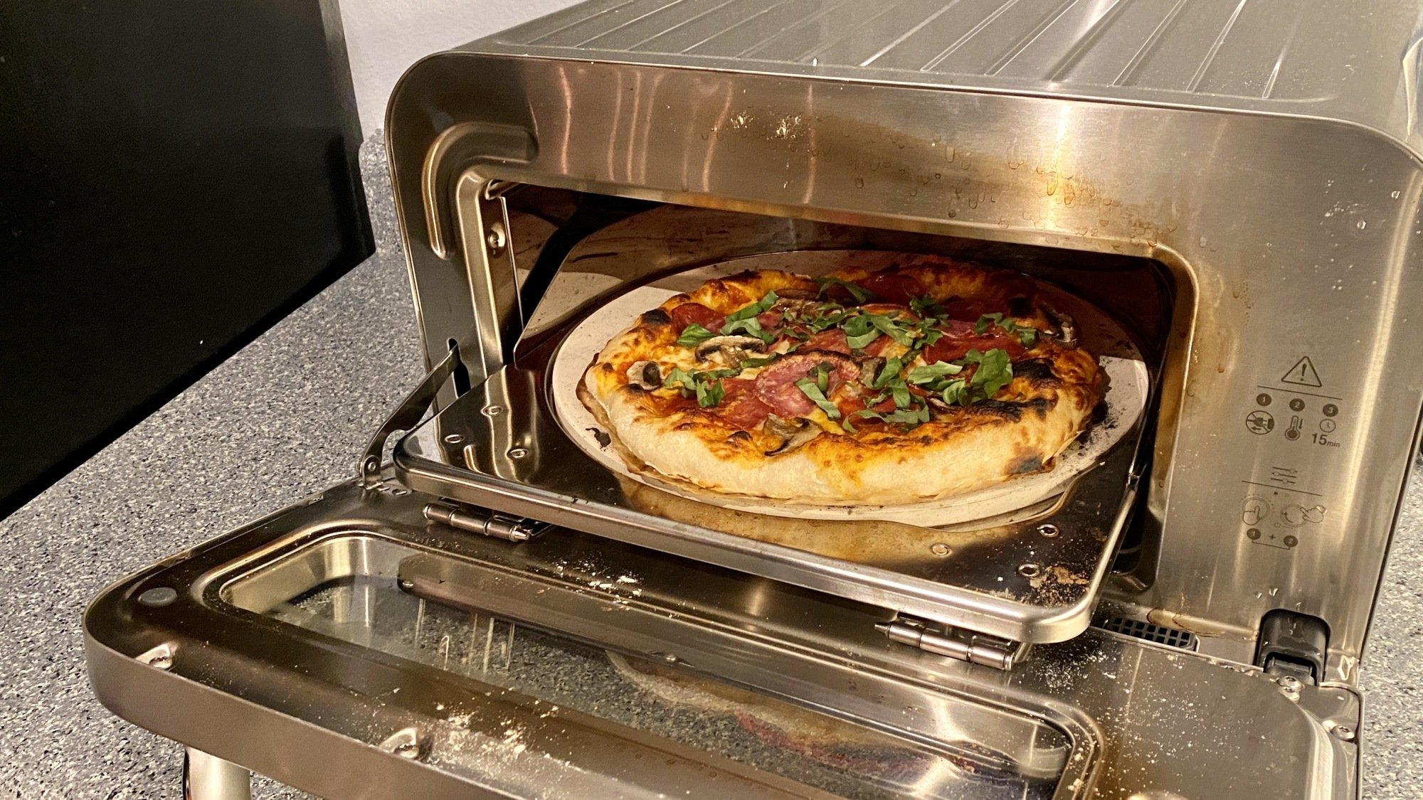 A pizza oven is open with a pizza inside. The pizza oven has some staining and discoloration on the inside of the door.