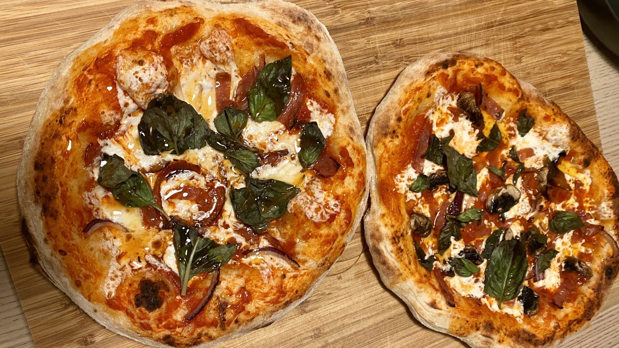 Two perfectly cooked, golden-brown pizzas on a wood cutting board