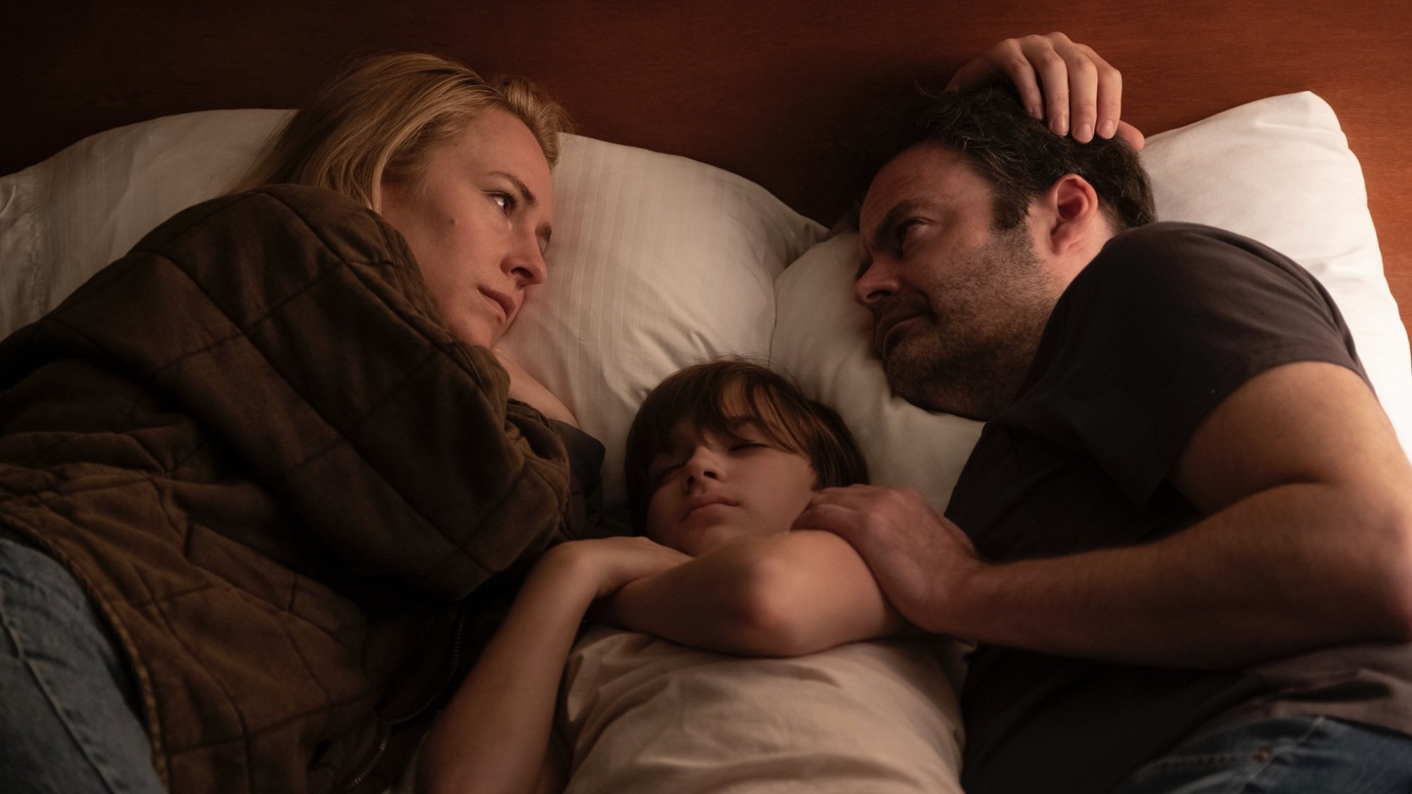 Sally Reed and Barry Berkman lie on a bed facing each other with their son John between them.