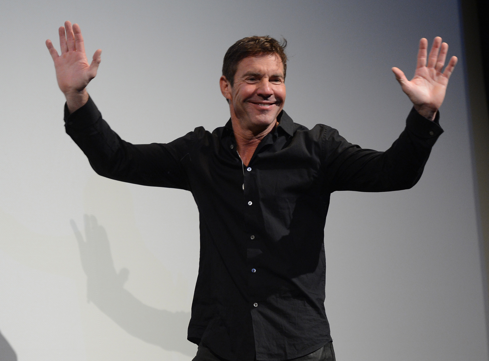 Dennis Quaid with his hands raised above his head. 