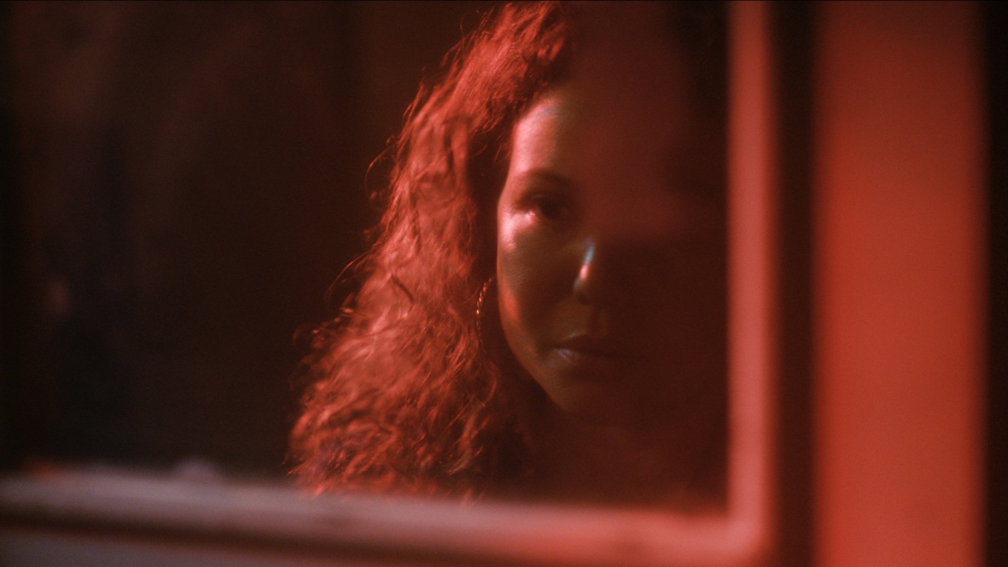 A woman bathed in red light looks through a window.