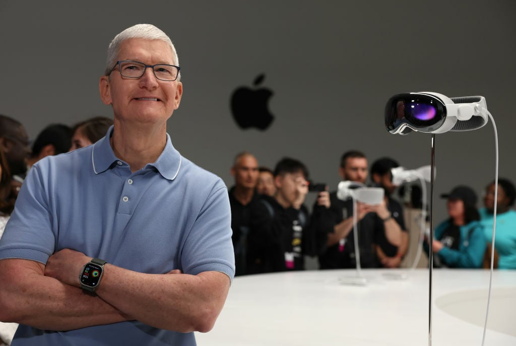 Apple CEO Tim Cook posing next to the Vision Pro headset