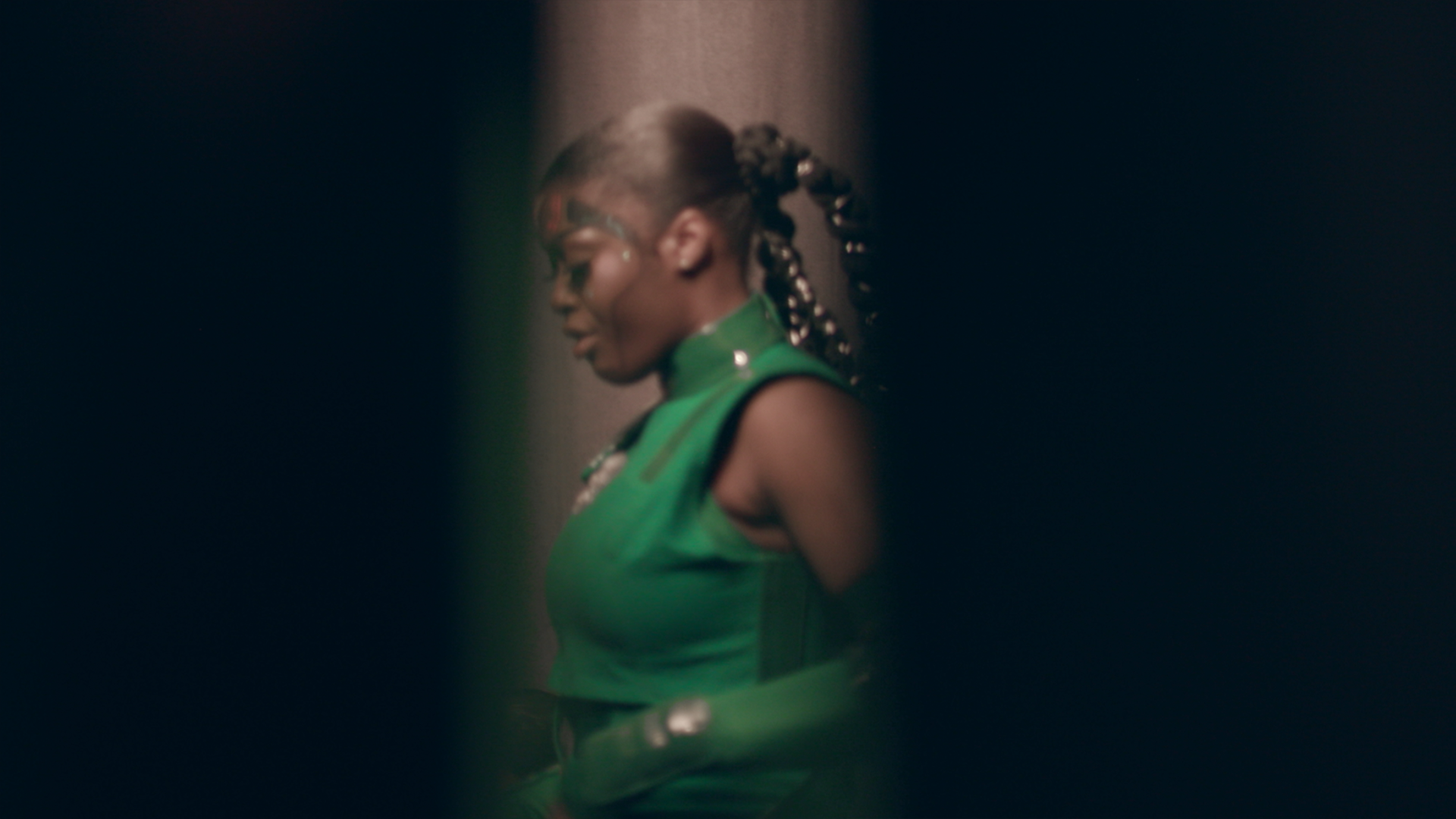 Rapper Tierra Whack dressed in a futuristic green outfit with braids entwined with gold material down her back.