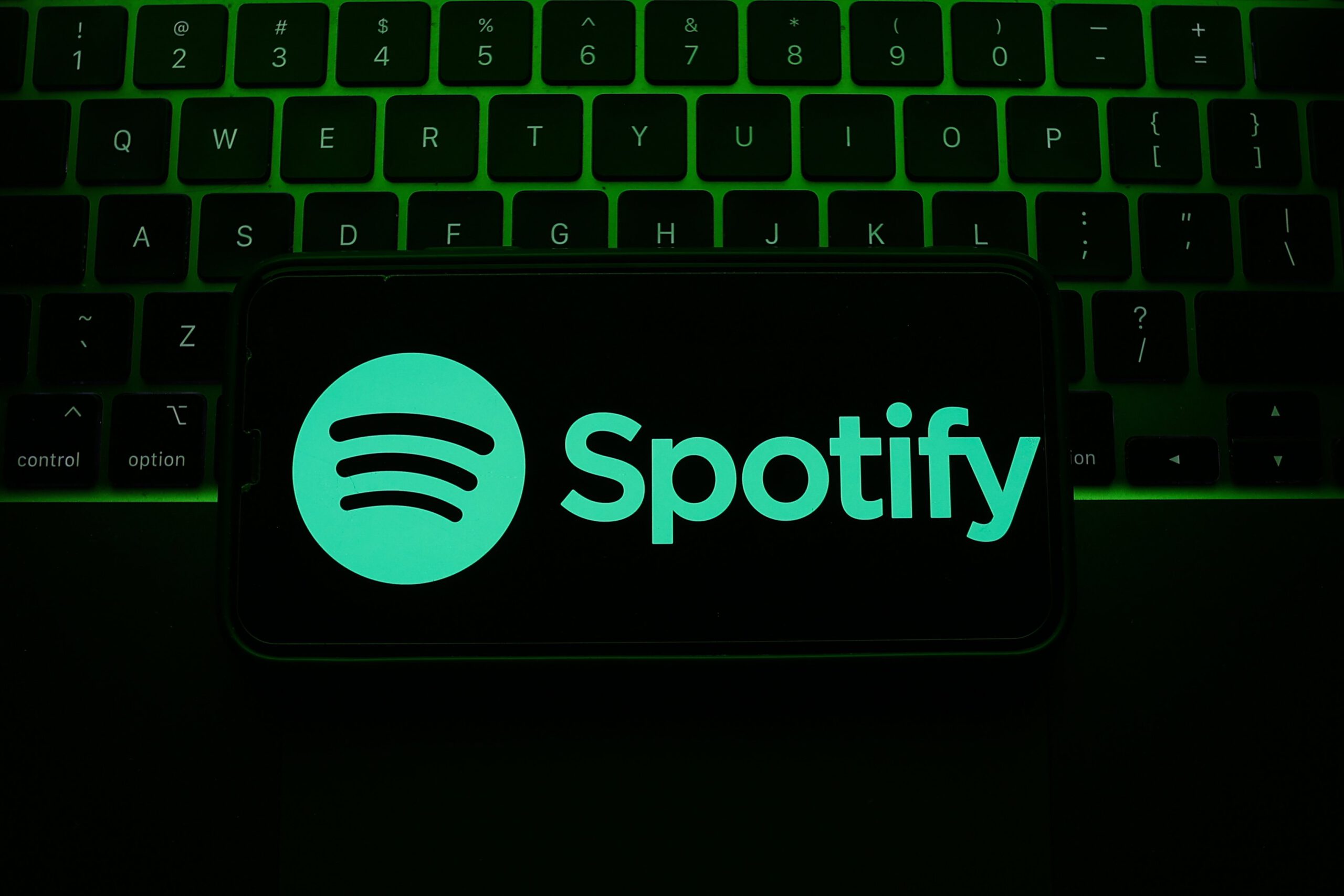 A laptop keyboard and Spotify logo displayed on a phone screen are seen in this illustration photo.