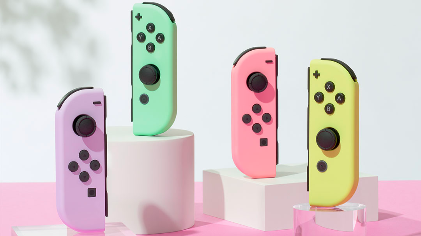 the pastel nintendo switch joy-cons upright on white and clear stands against a pink backdrop
