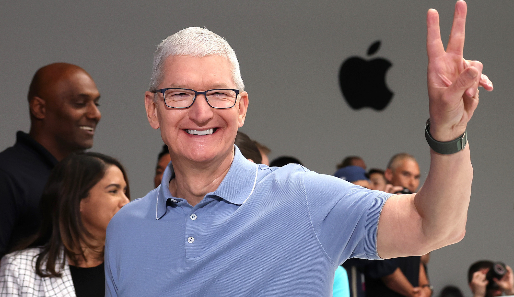 Tim Cook in front of an Apple logo flashing a peace sign