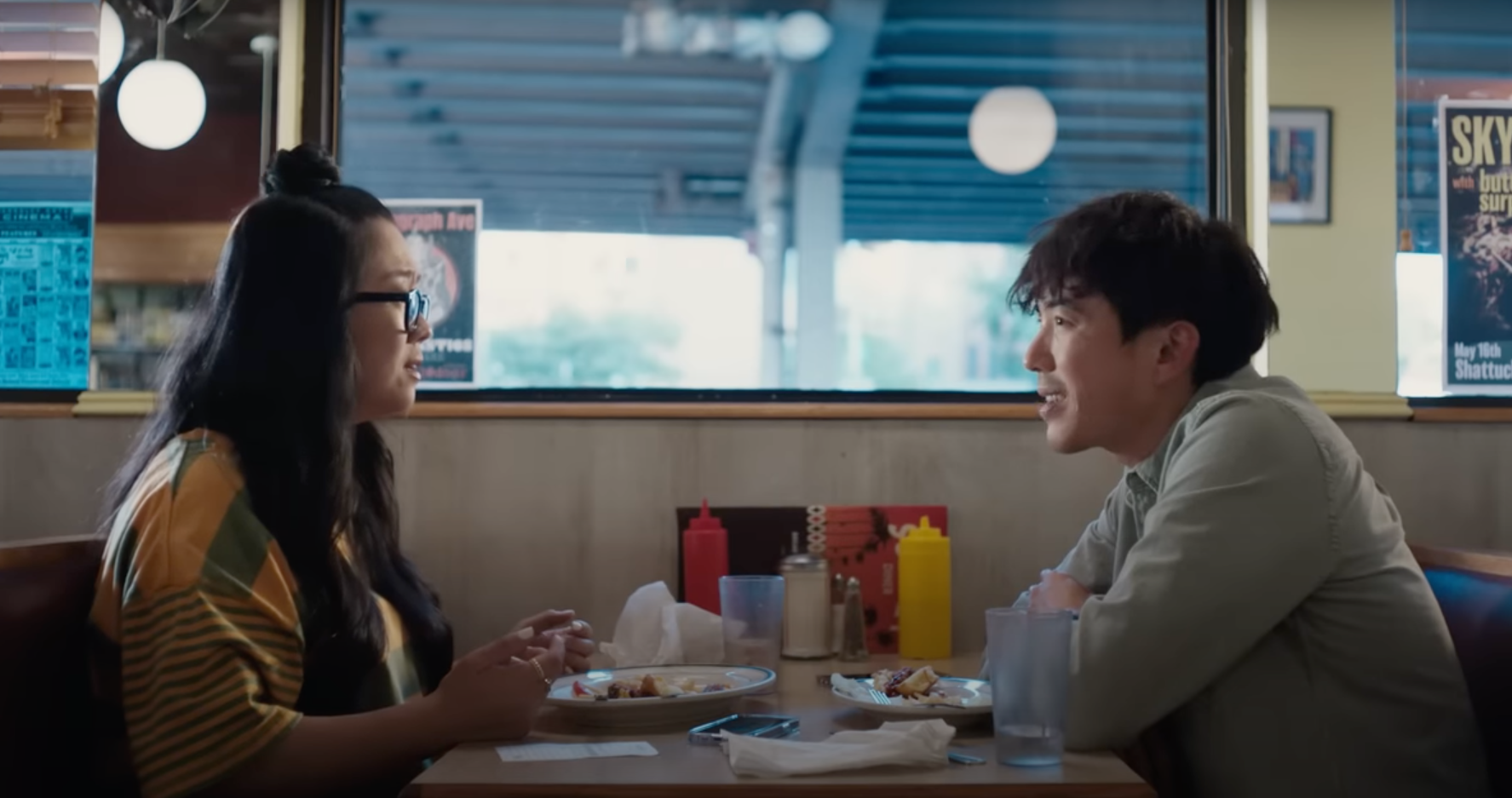 Two people, a man and a woman, sit across from one another at a diner table