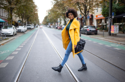Woman walking across the street with yellow jacket and black shoulder bag