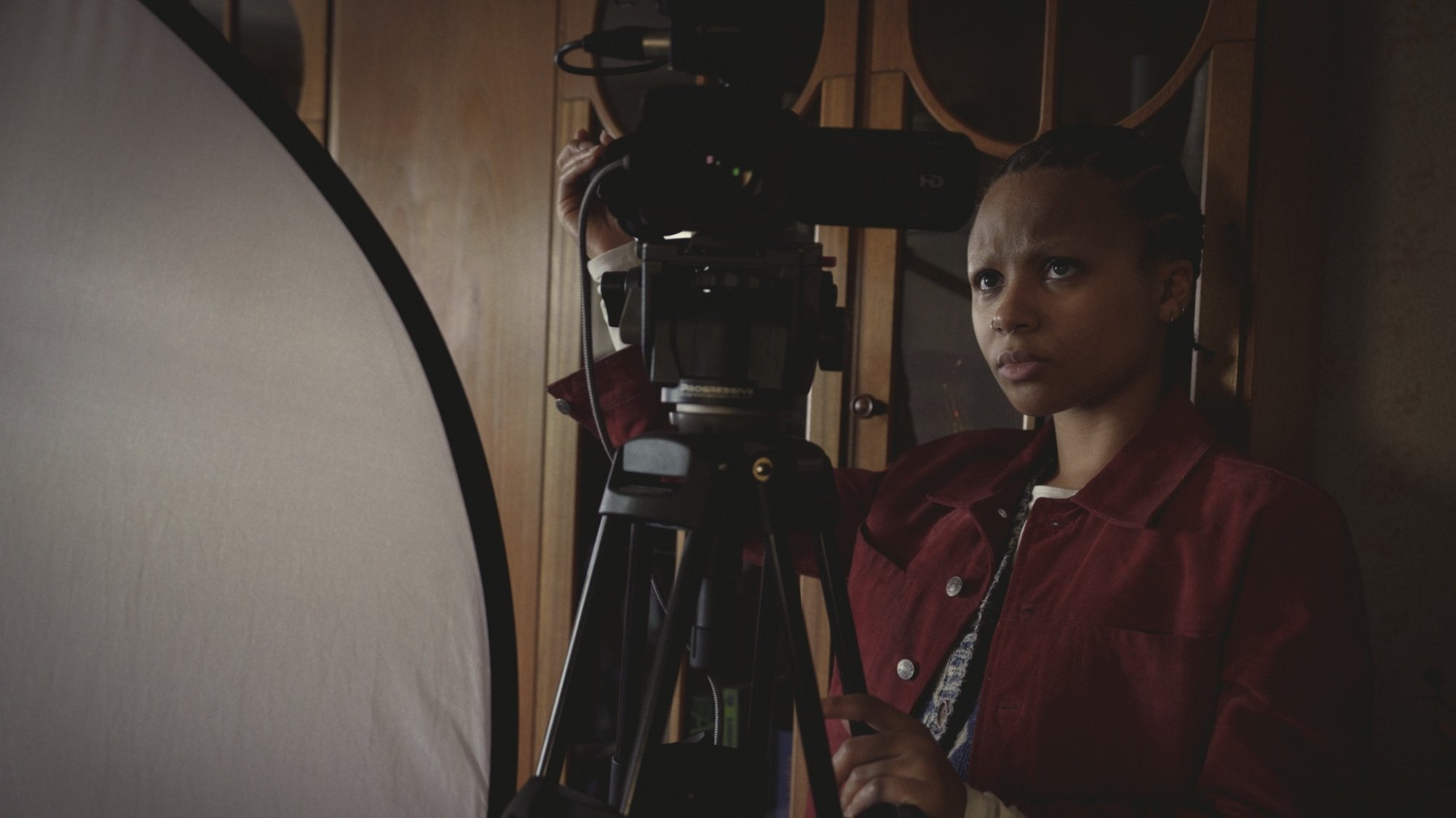 A young woman in a red shirt stands behind a camera.