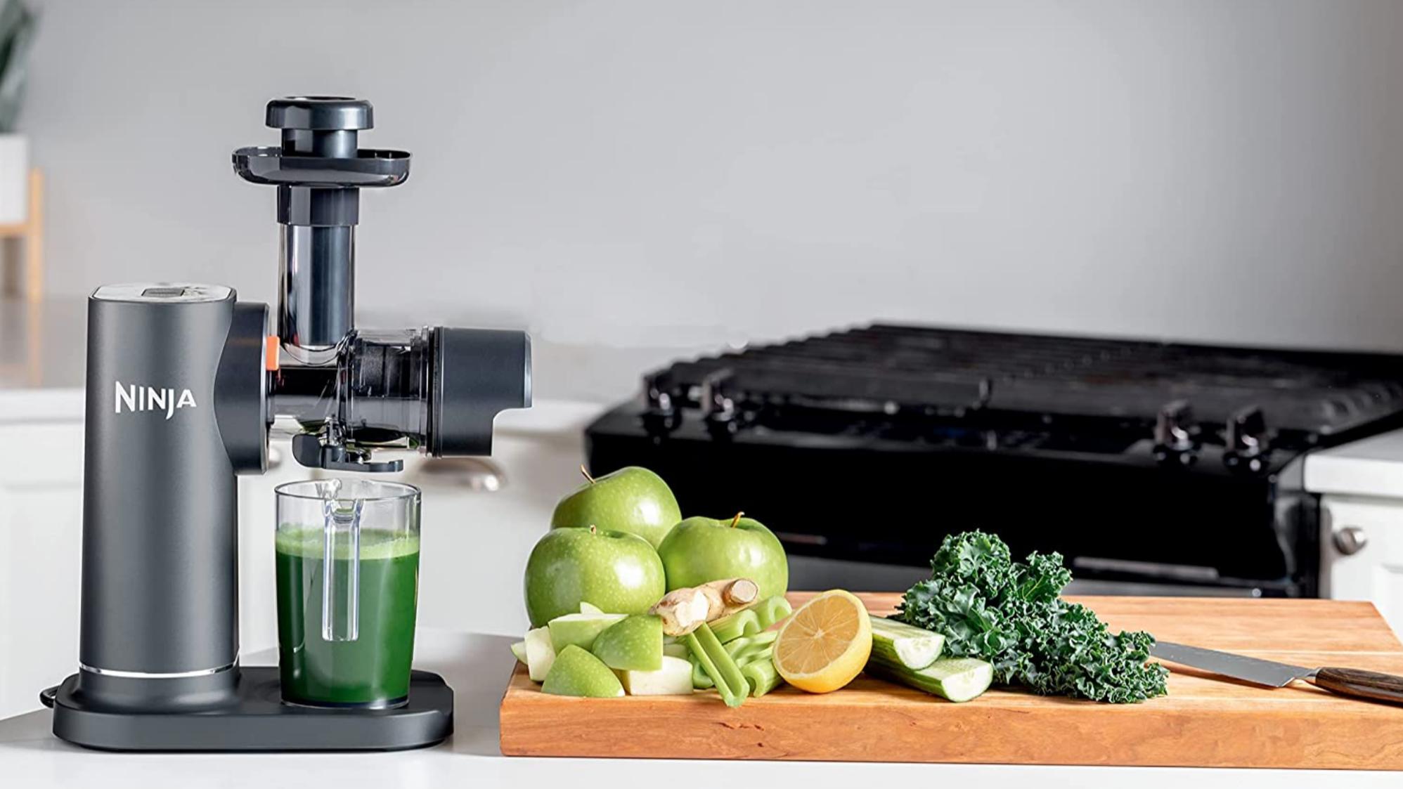 ninja neverclog cold press juicer to the left. green apple, orange, kale, and cucumber to the right.