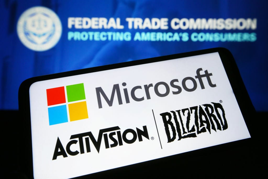 Microsoft and Activision Blizzard logos are seen on a smartphone in front of the Federal Trade Commission (FTC) logo on a PC screen. 
