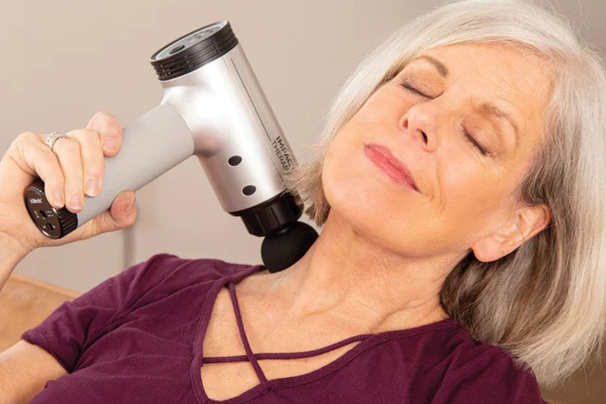 A woman with her eyes closed using the truRelief percussive massage gun on her lower side neck.