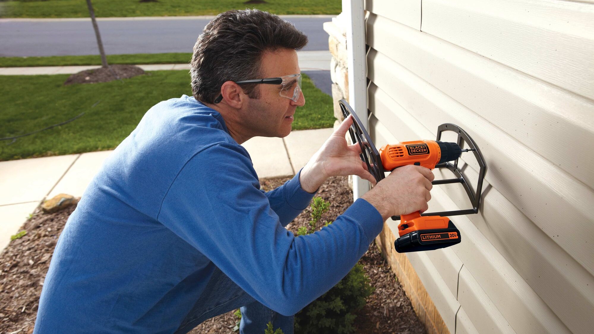 middle-aged man using black and decker cordless drill on outside of home