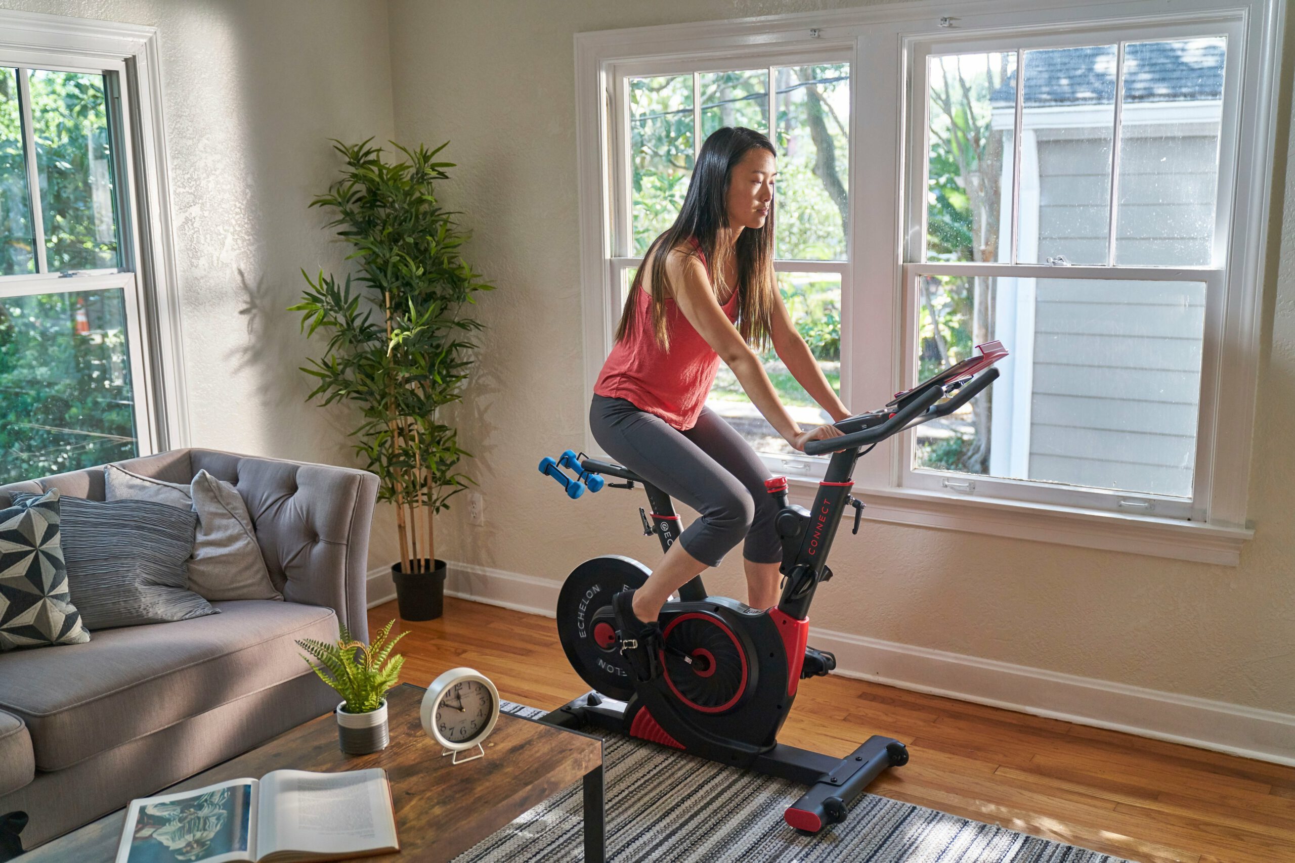 A woman riding an Echelon EX-3 bike in her living room in front of some windows