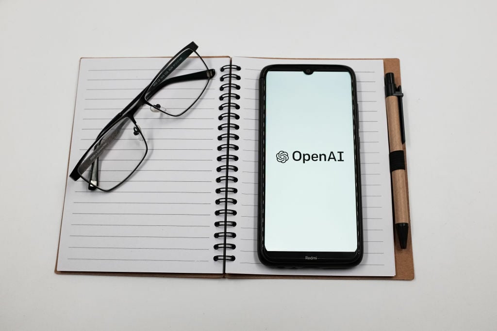 OpenAI logo on a smartphone on a notebook next to a pair of eyeglasses