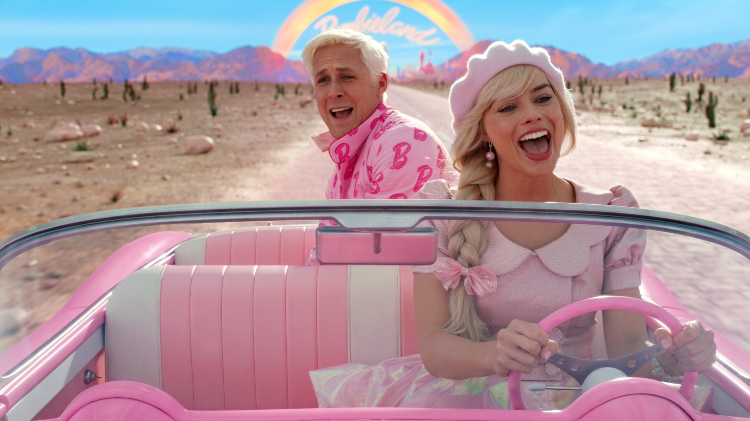 A man and woman wearing pink drive in a pink convertible. 