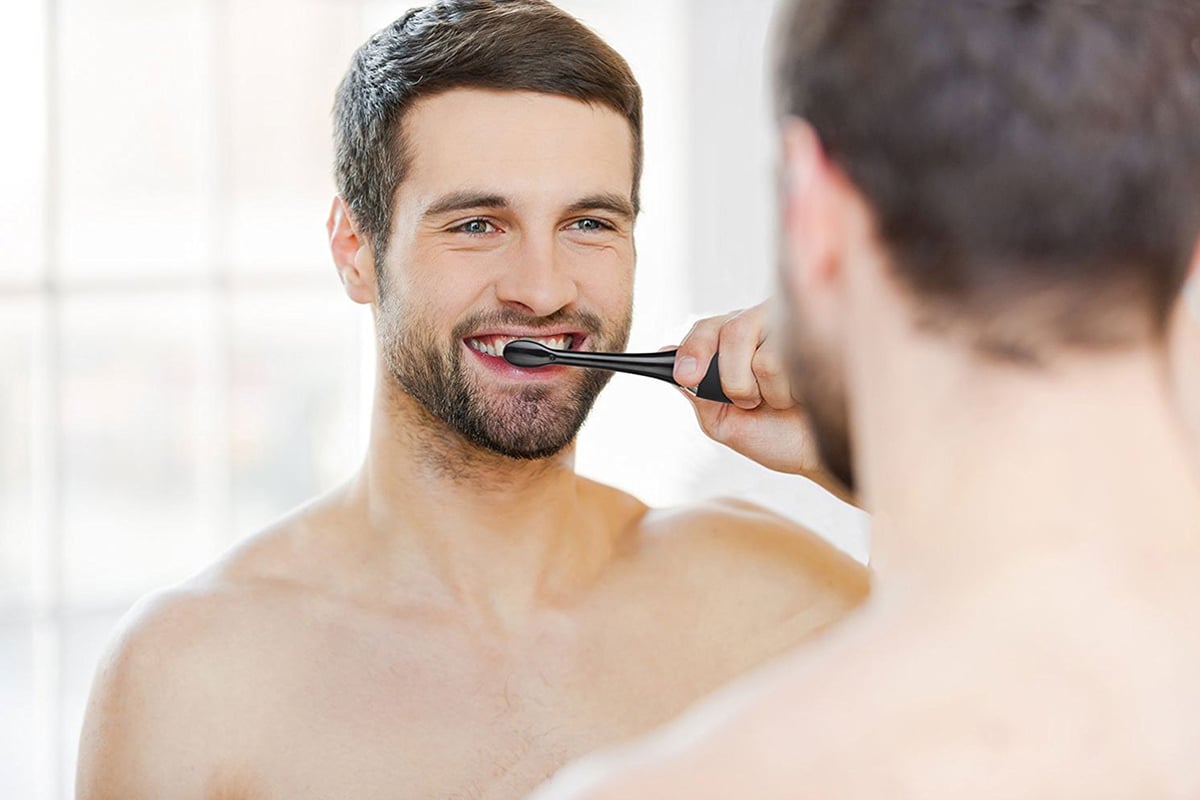 man brushing his teeth in the mirror