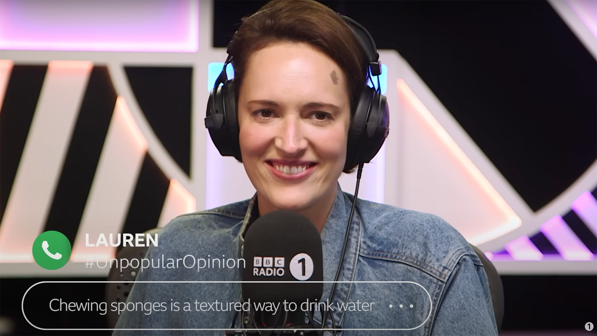 A woman sitting on a radio show wears headphones and grins.