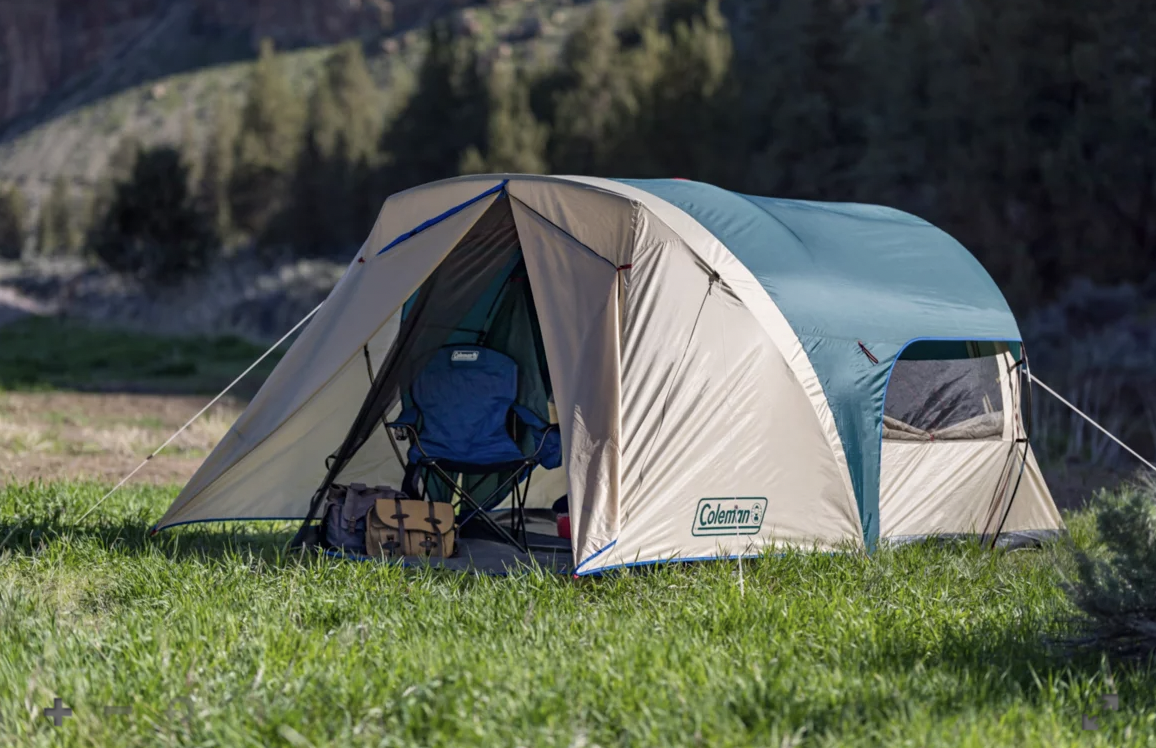 The Coleman 6-Person Cabin Tent resting on a patch of grass with chairs and equipment inside it 