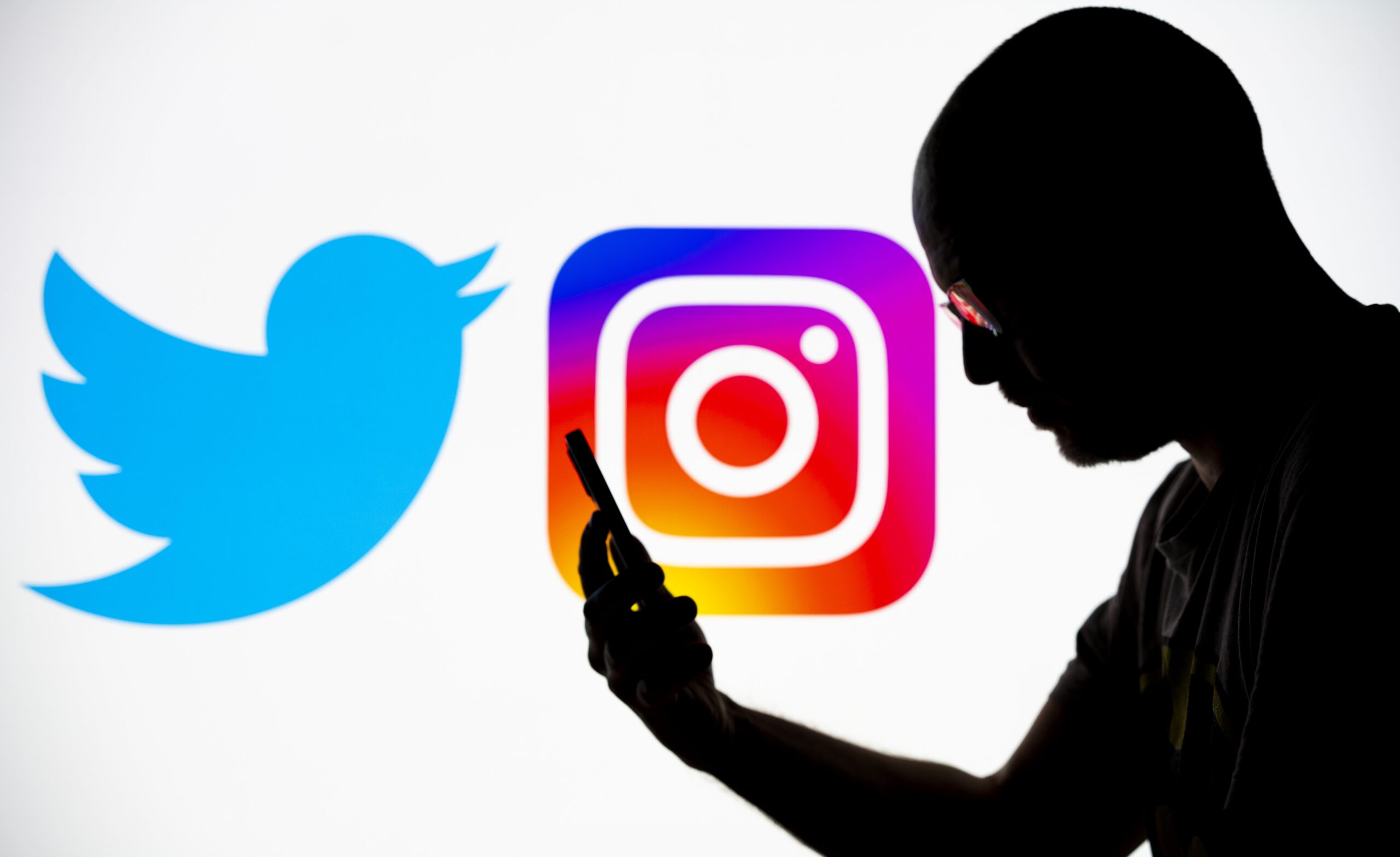 A figure looks at a phone in silhouette, with the Twitter and Instagram logos displayed in the background.