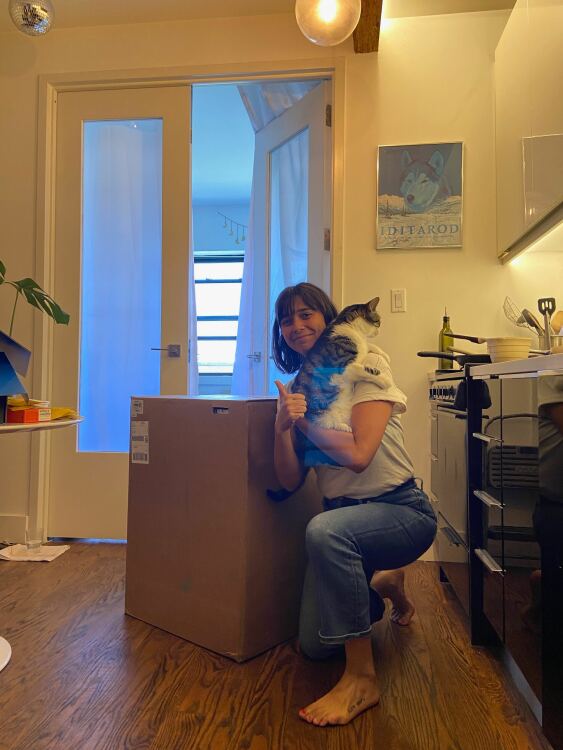 A person holding their cat next to a big box with a Litter-Robot 4 inside.