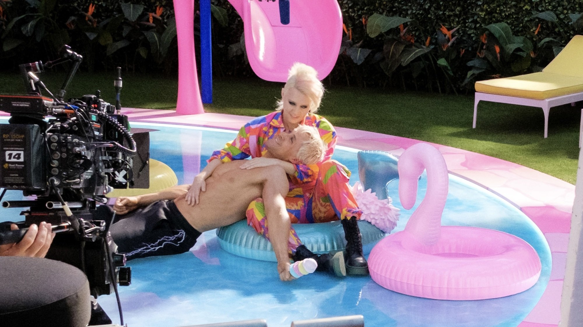 Ryan Gosling as Ken lies shirtless in Kate McKinnon as Barbie's lap. The two float on a fake blue pool.