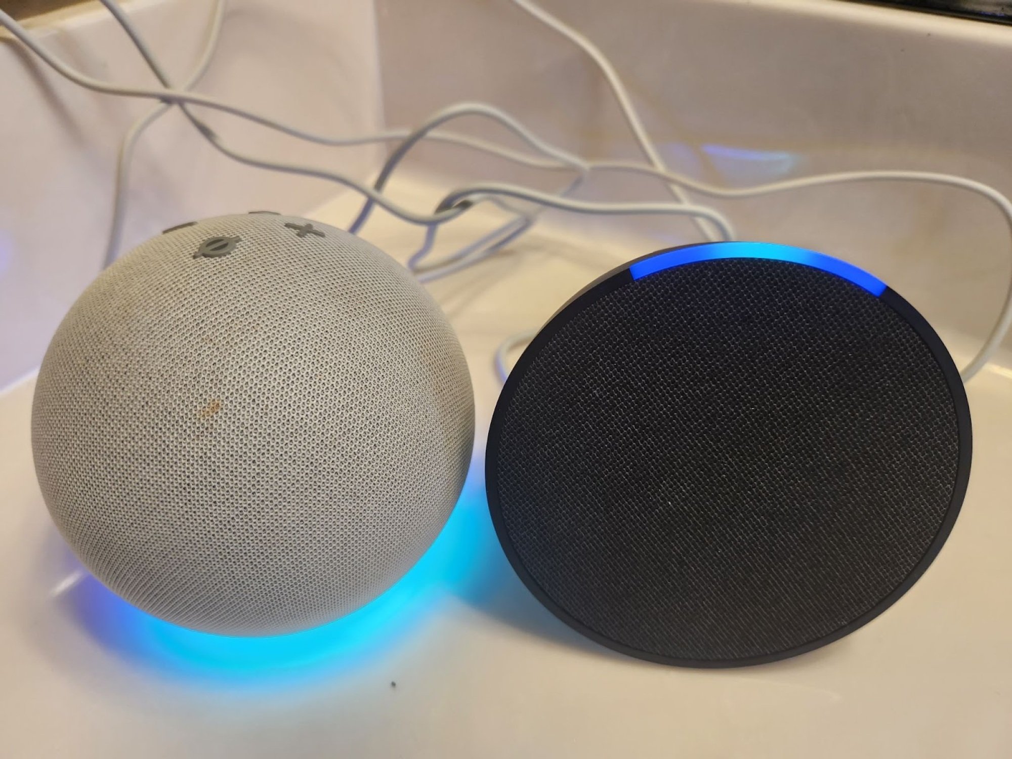 round, gray echo dot speaker next to flat, circular echo pop speaker. both are similar in size