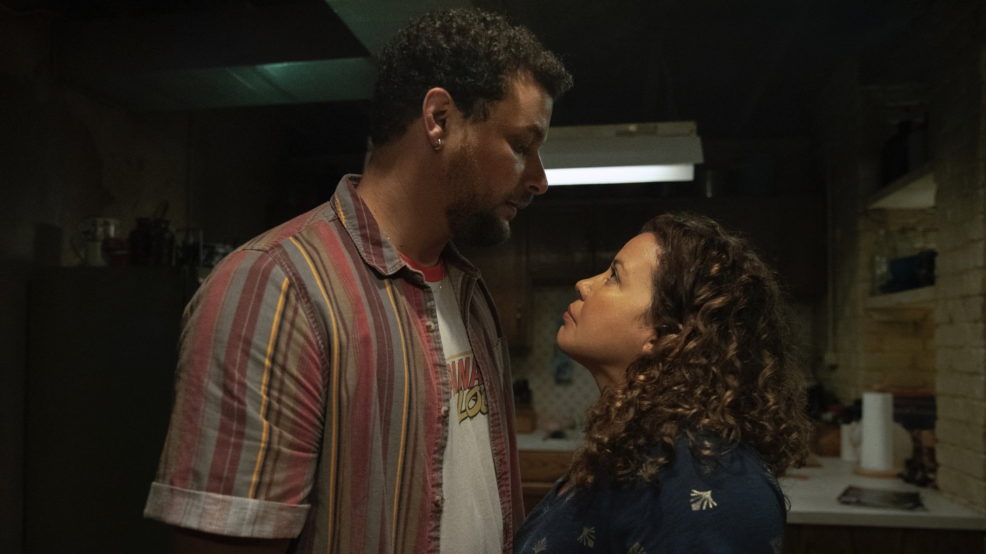 A man and a woman stand toe to toe looking at each other in a basement apartment.