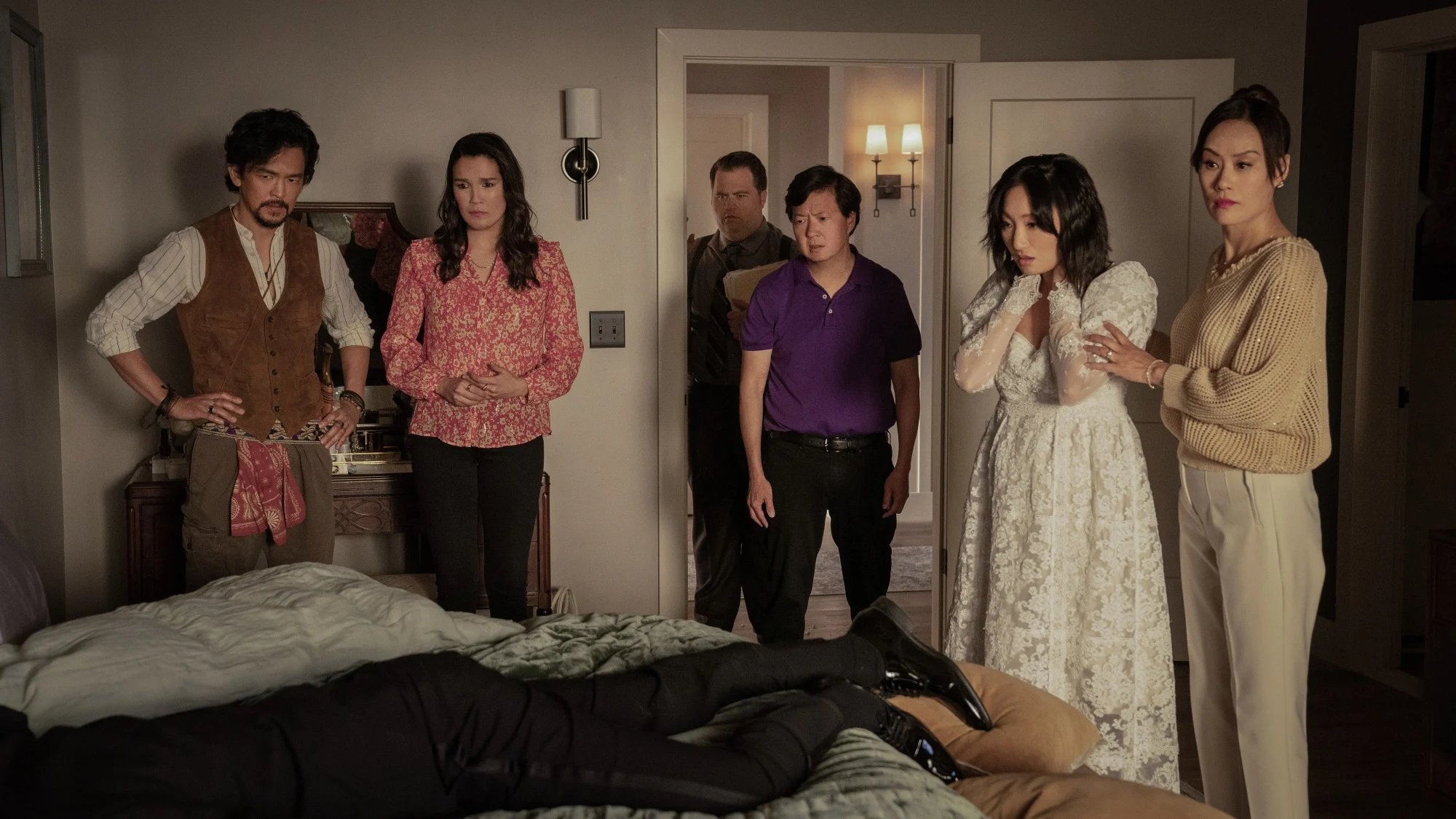 A group of friends stand in a room around a dead body. 
