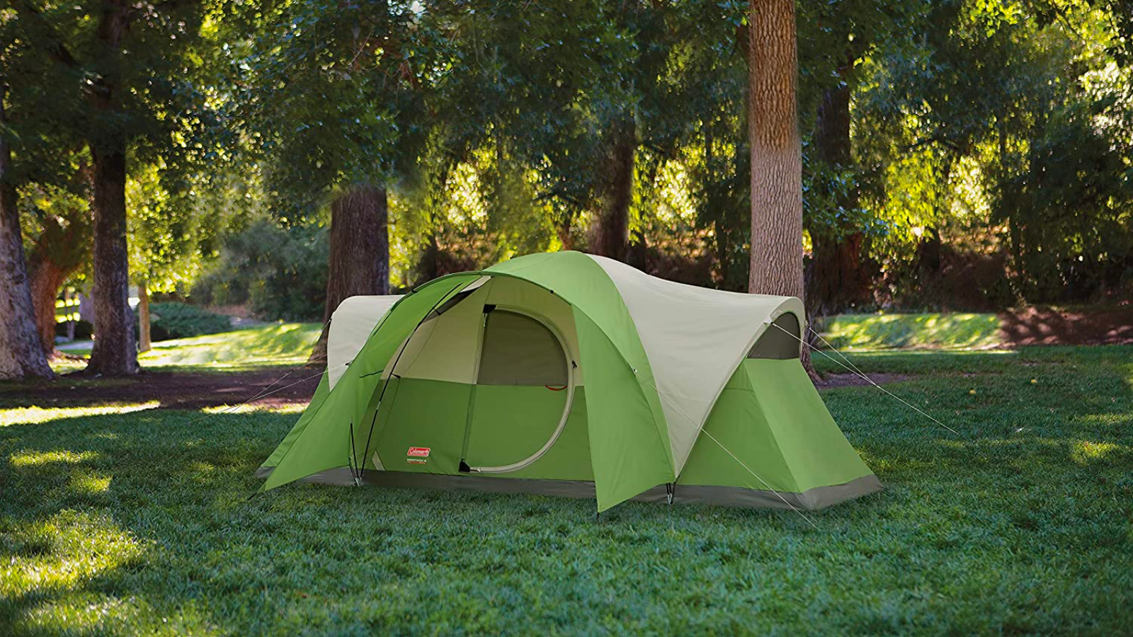 a green coleman montana 8-person tent set up on a grassy lawn in front of tall trees