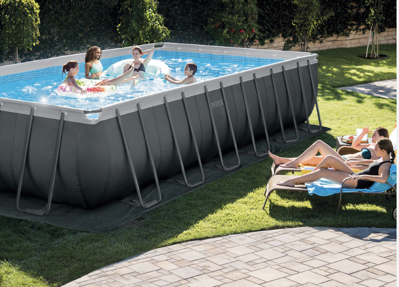 The Intex Ultra XTR pool standing on someone's lawn, with people swimming in it while others sunbathe nearby