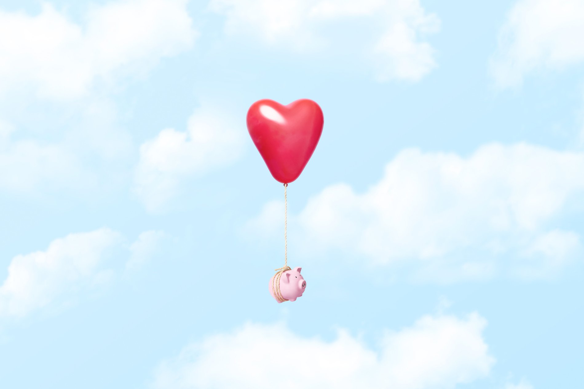 Piggy bank tied to a red heart ballon in clouds
