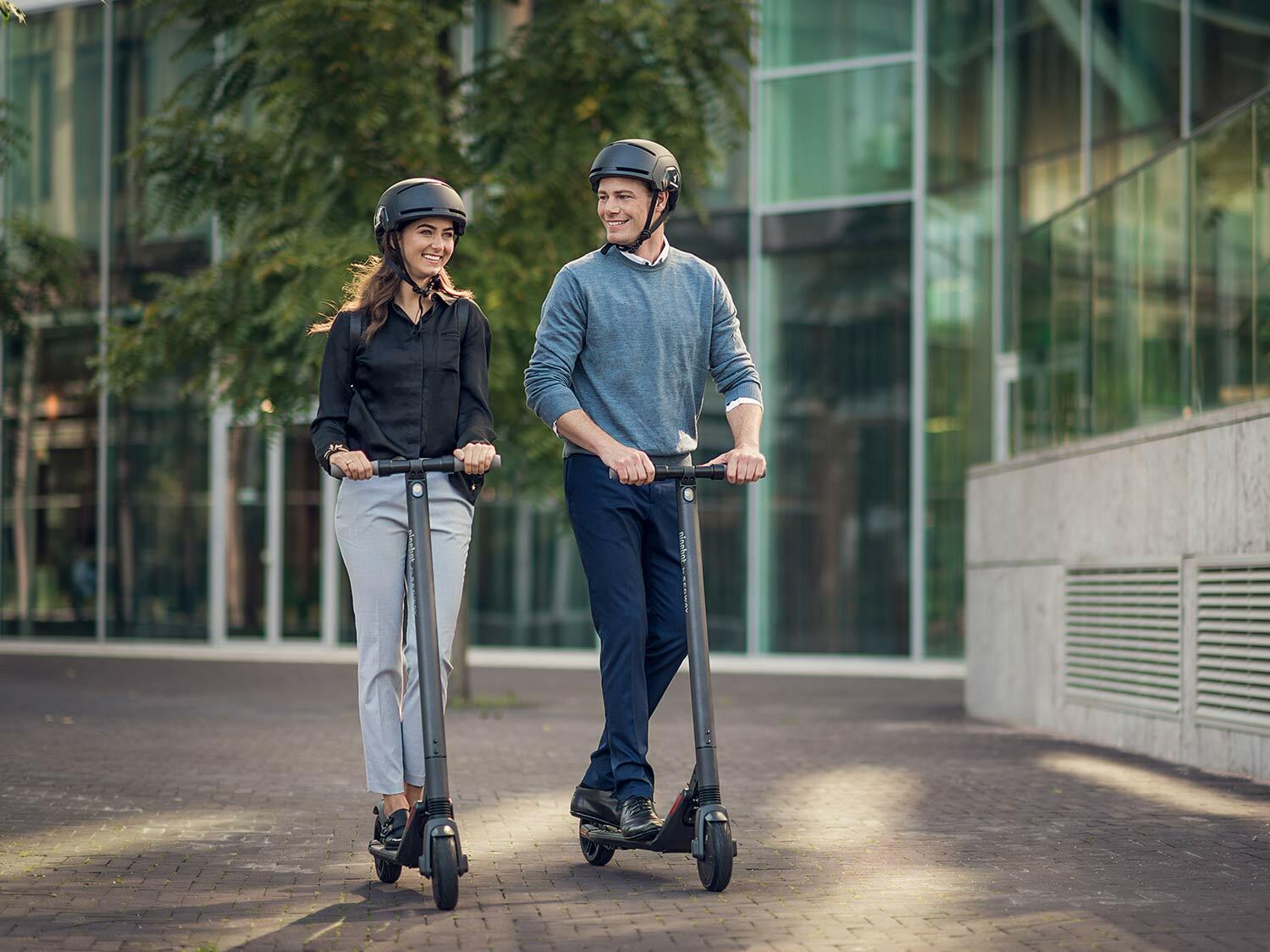 Two people riding the Segway Ninebot KickScooter ES2 with helmets on.