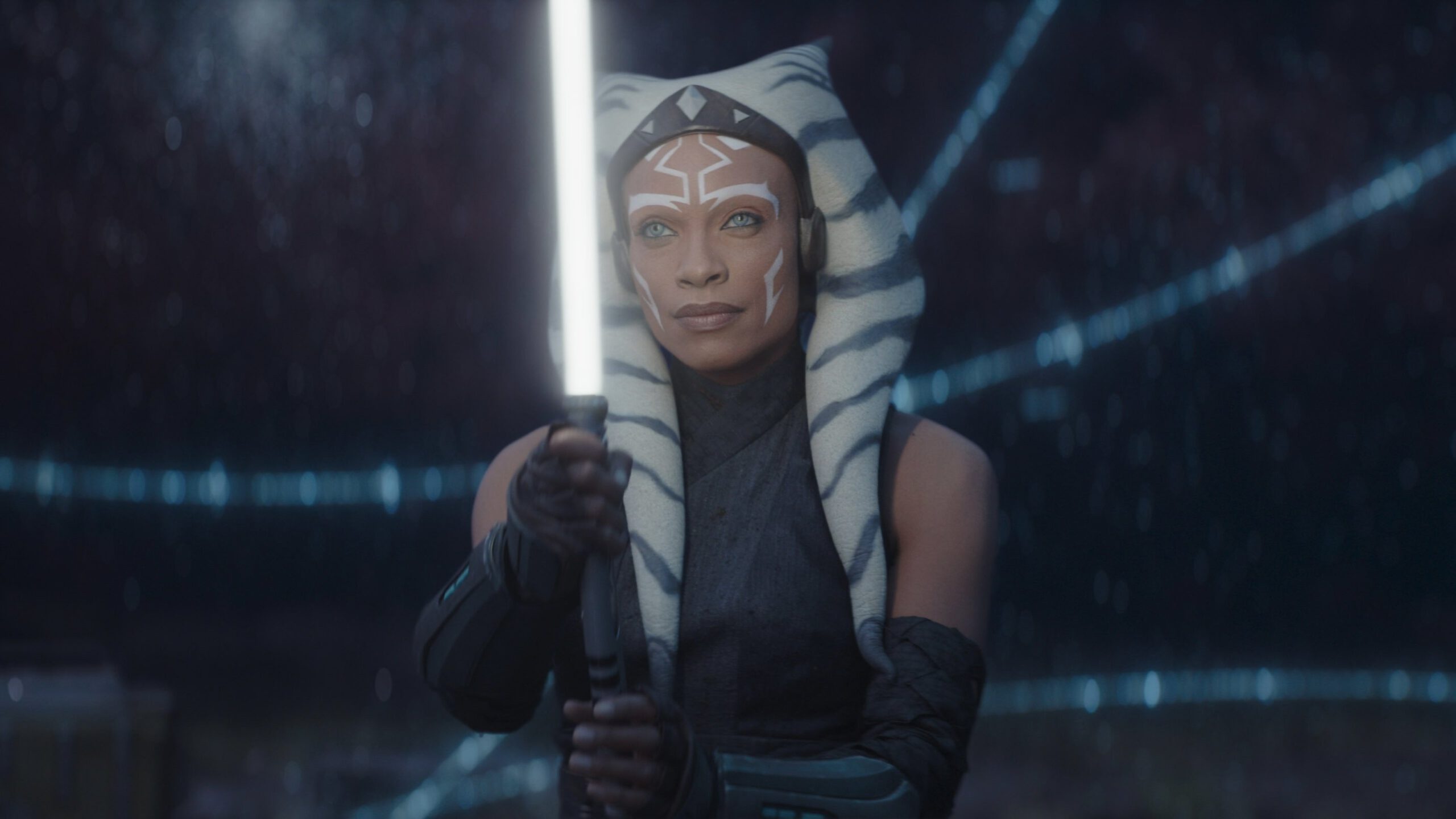 Ahsoka Tano wields a white lightsaber while surrounded by a blue hologram of a star map.