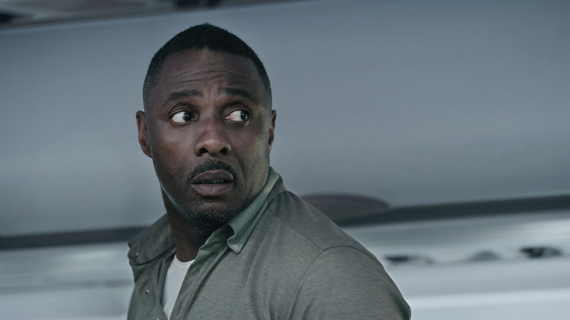 A man in a green shirt turns around, worried, in the aisle of an airplane.