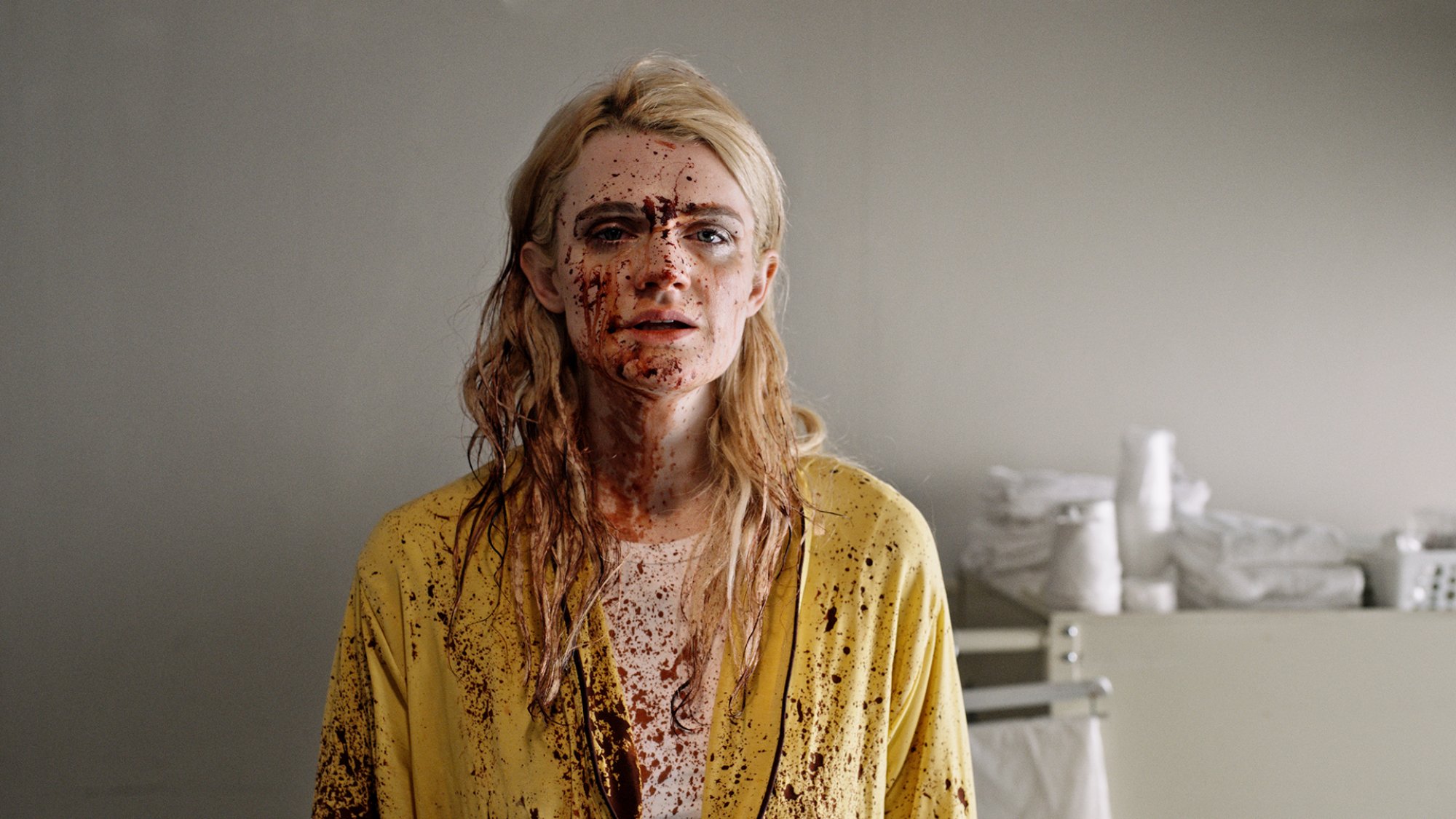 A woman stands in a room covered in blood spatters.