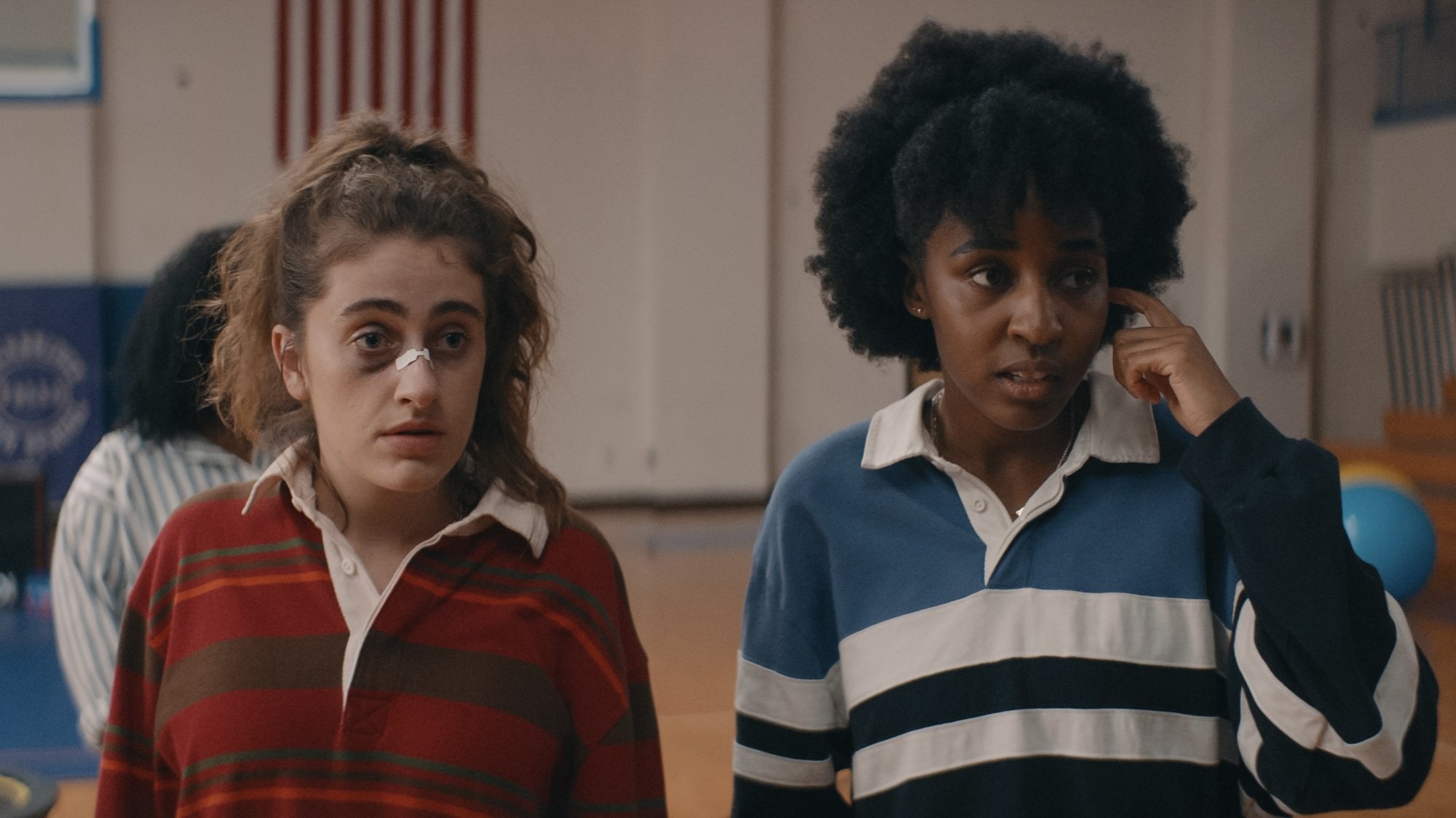 Two young woman with bruised faces standing in a high school gym.