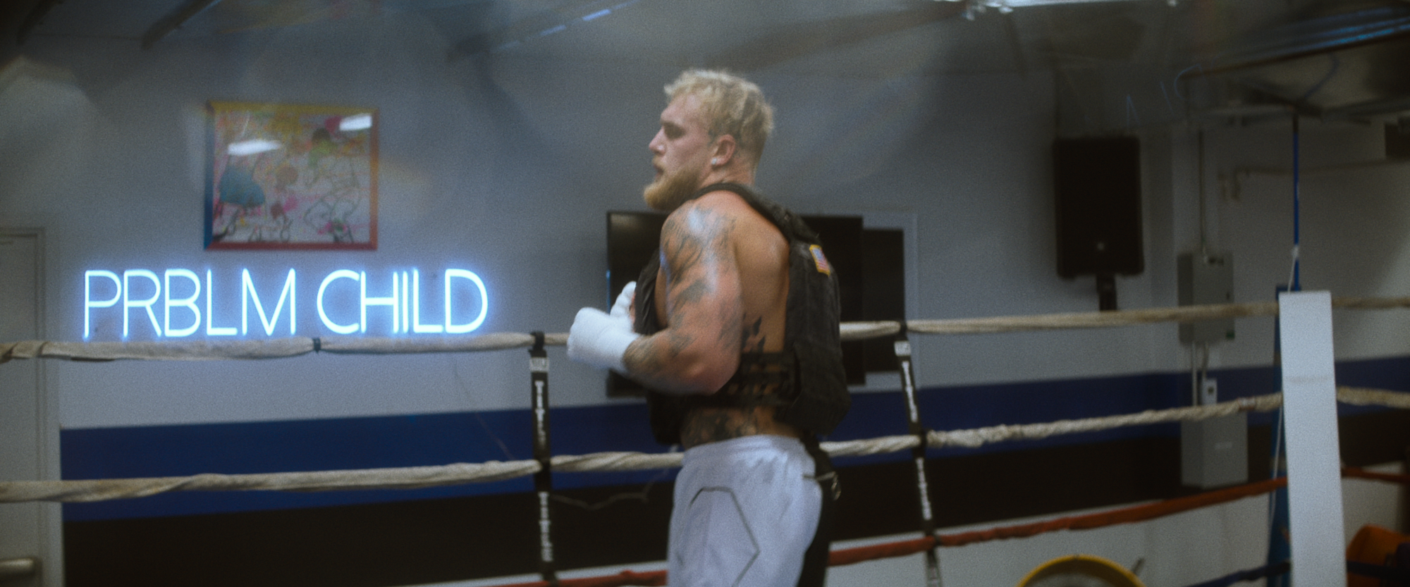 Jake Paul in the boxing ring at the gym. Behind him a neon sign reads "PRBLM CHLD."