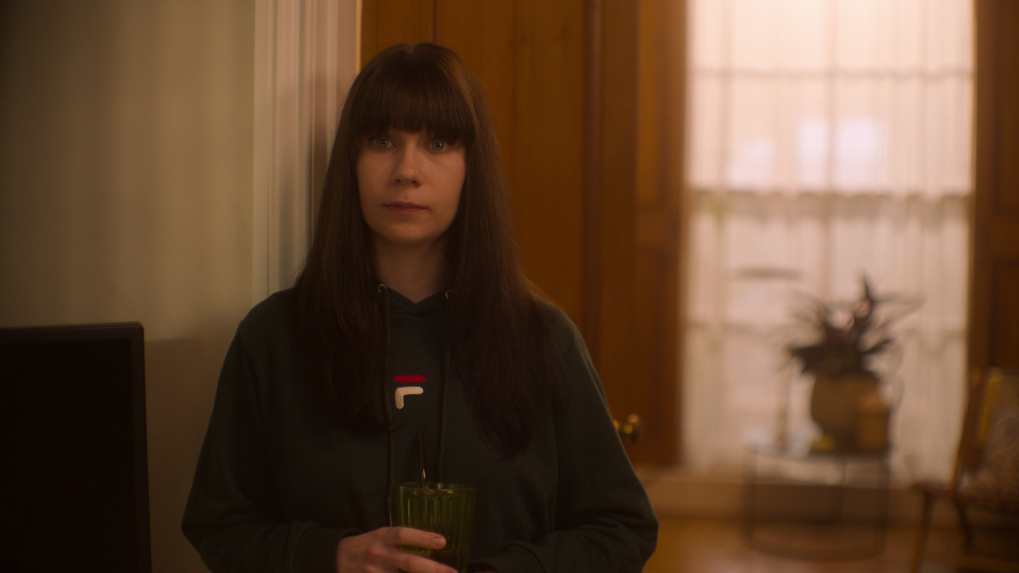 In the TV series "Heartstopper" Jenny Walser plays Tori, standing in a living room holding a glass.