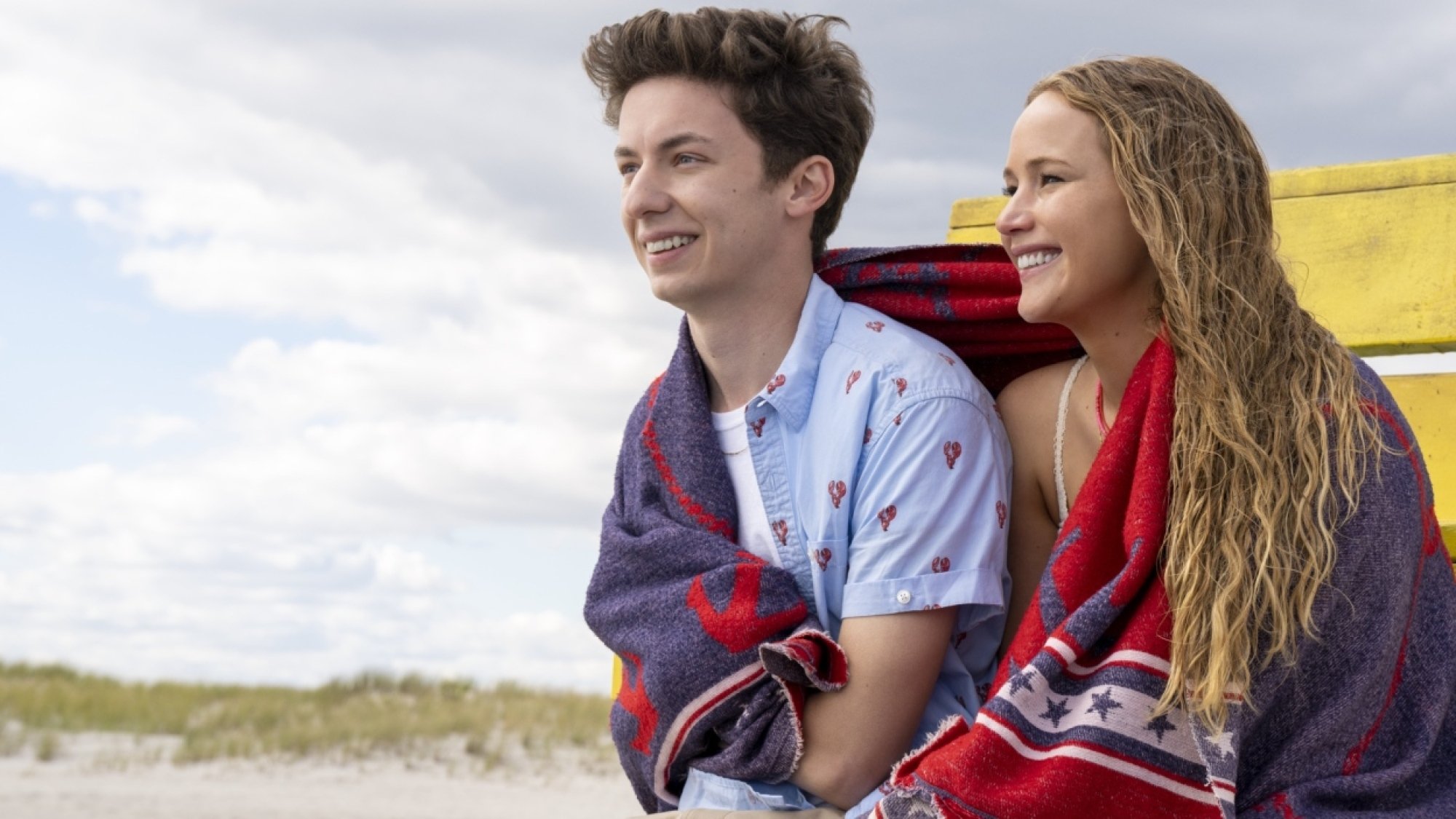 A woman and a teenage boy laugh by the beach. 