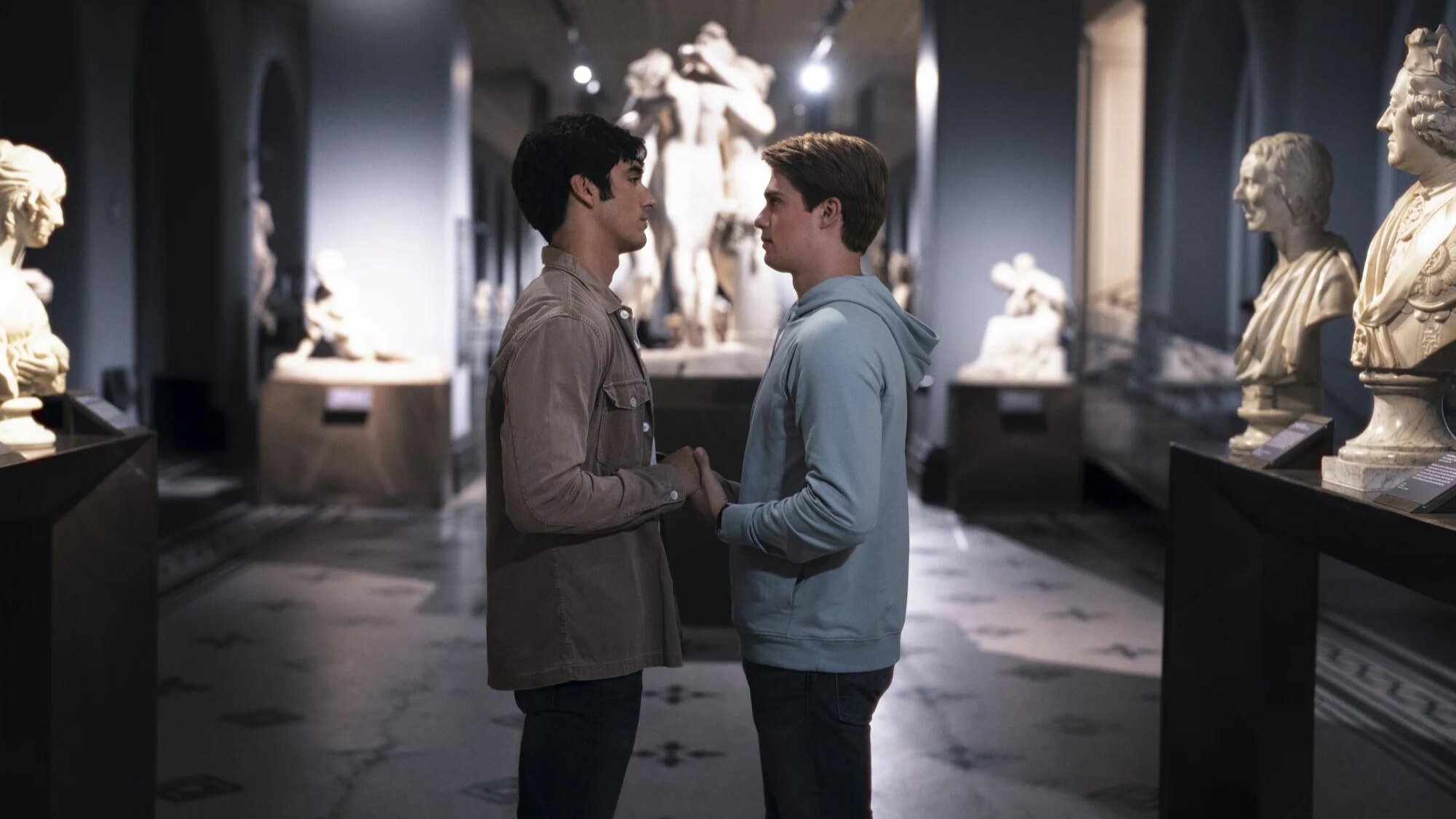 Two men hold hands in a museum. 