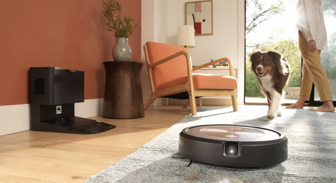 The Roomba Combo j9+ vacuum in a living room setting, next to its base, a family dog, and a woman