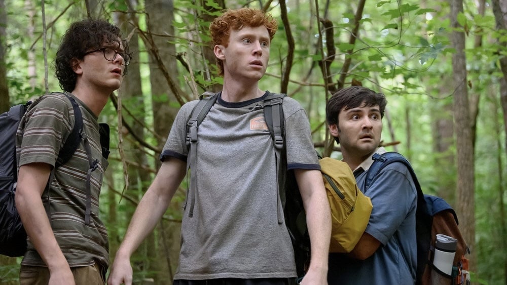 Three young men hike through the forest.