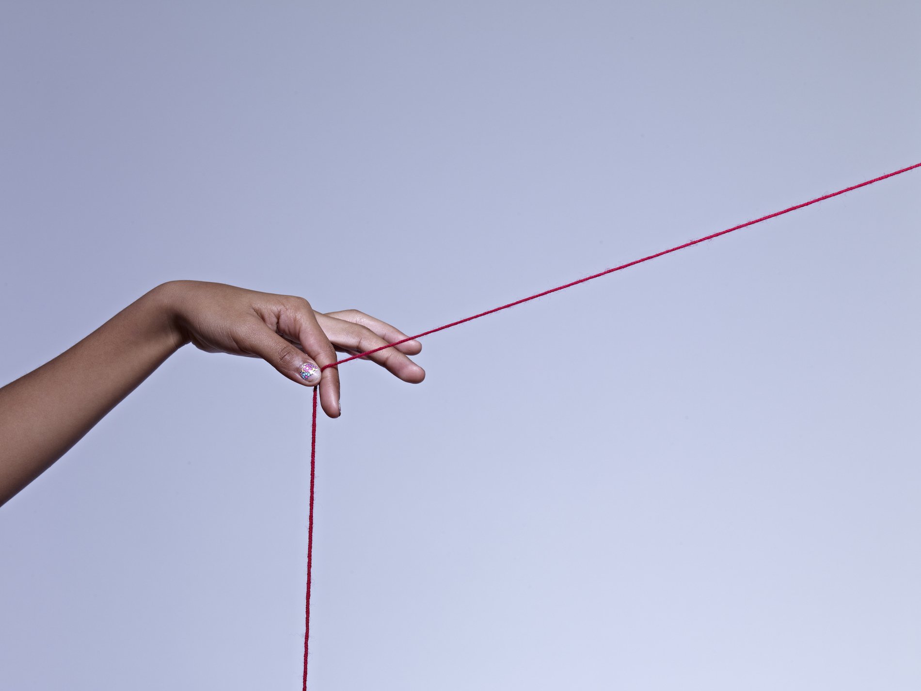 A woman's hand holds a piece of red string. 